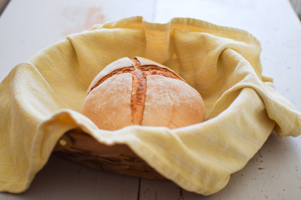 Beautifully baked sourdough boule in a basket with a yellow cloth