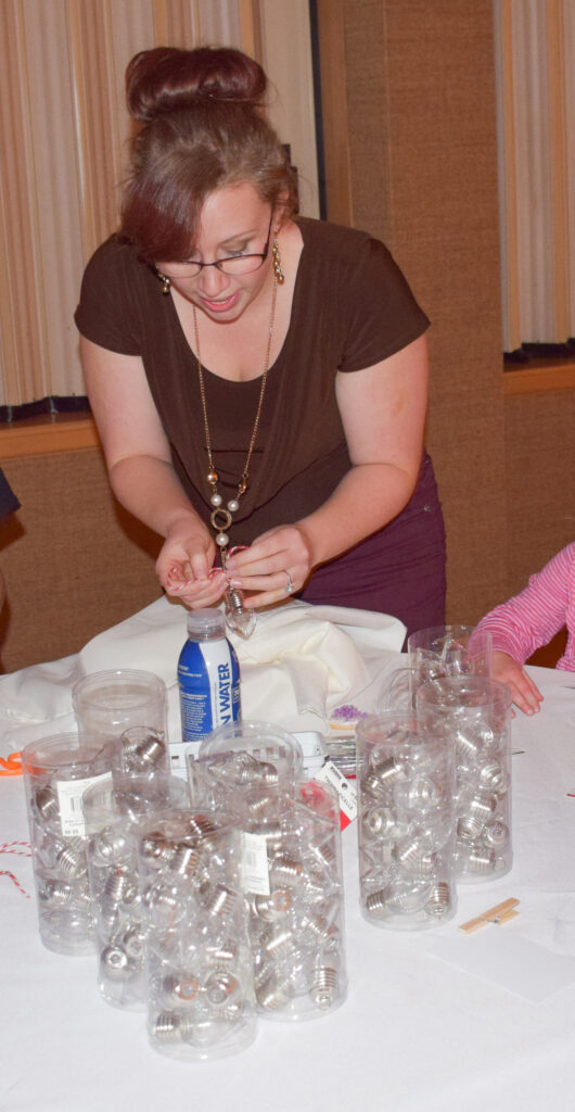 Lady helping kids make ornaments shaped like a lightbulb